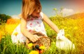 Girl petting Easter bunny on meadow with eggs