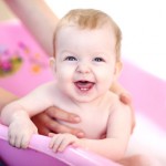 Mother washing a smiling baby in pink bathtub