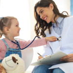 Little girl at the doctor for a checkup. Child auscultate the heartbeat of the doctor.