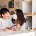 Preschooler Kid playing tetris wood puzzle with teacher educador help using face mask for coronavirus pandemic. Homeshooling. Learning Community. Montessori School