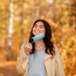 End of coronavirus epidemic concept. Millennial pregnant woman removing medical mask at autumn park