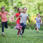 A group of happy children of boys and girls run in the Park on the grass on a Sunny summer day . The concept of ethnic friendship, peace, kindness, childhood.
