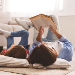 Little girl and father enjoying book together, laying on floor