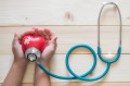 Young child kid holding red love heart hand exercise ball with bandage, MD medical doctor physician's stethoscope on light white wood background: Nursing children day care healthcare support concept