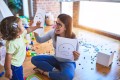 Young beautiful psicologist and toddler doing therapy using emoji emotions at kindergarten