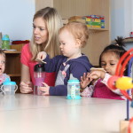 Erzieherin am Tisch Kinder trinken aus Trinkflasche mit Spielzeug