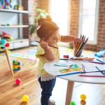 Beautiful toddler standing holding colored pencils at kindergarten