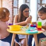 Young beautiful teacher and toddlers playing meals using plastic food and cutlery toy at kindergarten