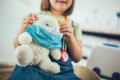 Soft toy bear with protective medical mask in child hands. Child playing doctor with soft toy.