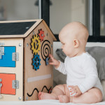 A child is playing with a wooden house. A special model of a house with many functions for the development of fine motor skills. Busy Board.