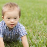 Down Syndrome child crawling in green grass